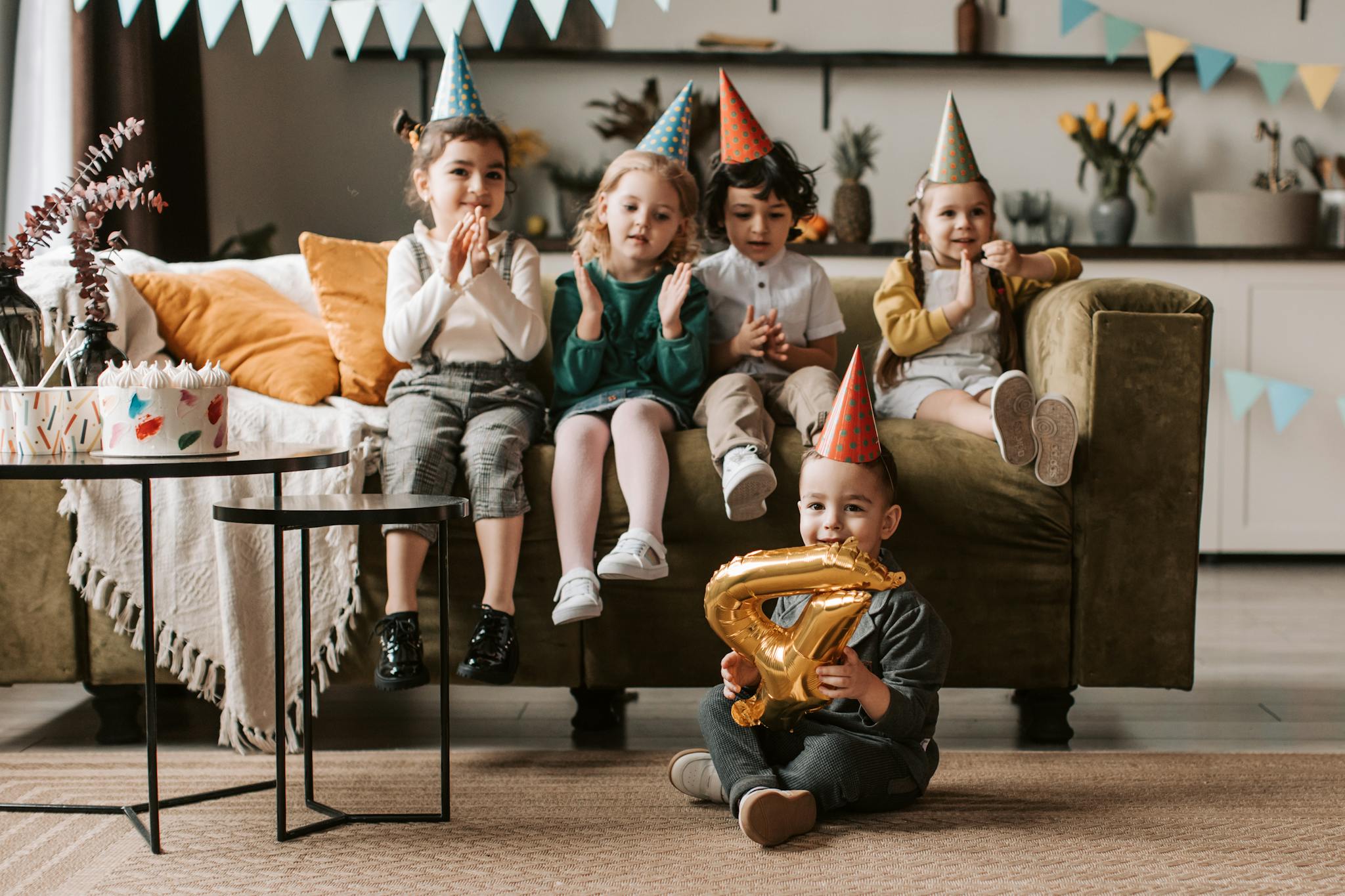 Happy children celebrating a birthday indoors with party hats and decorations.
