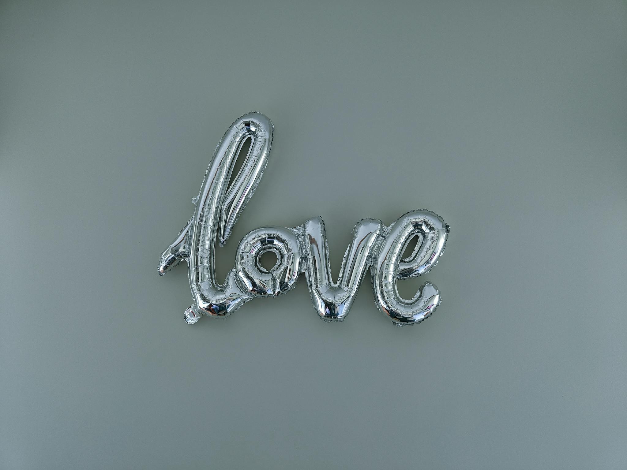 Metallic silver love balloon on a minimalist grey background, perfect for romantic themes and celebrations.
